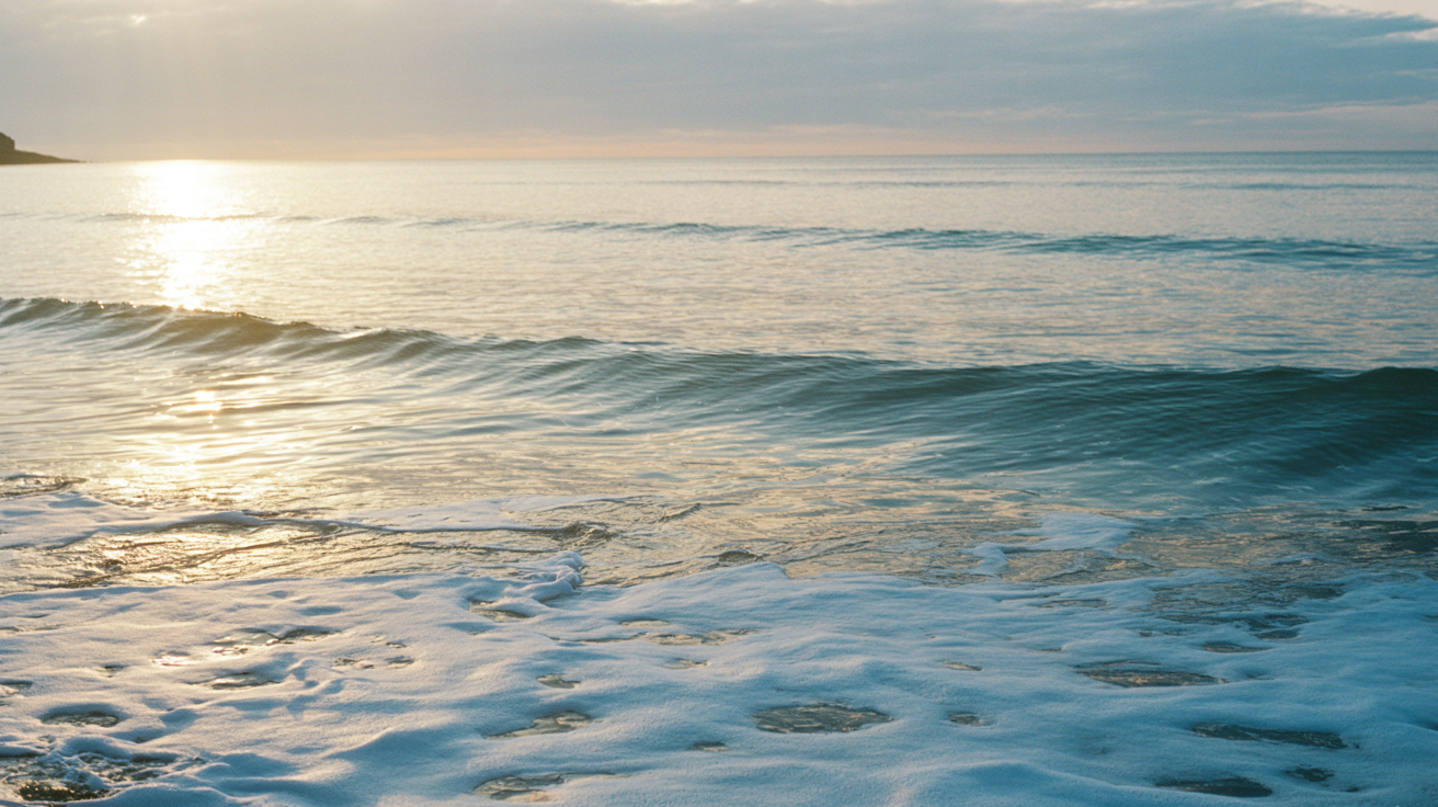 Glassy ocean surface at dawn with soft golden light reflections showing peaceful morning waves with mirror-like water texture and deep ocean blue with koa brown reflections