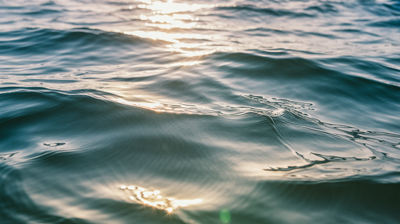 Close-up of ocean water surface with soft sunlight creating ripple patterns and light reflections showing therapeutic nature of water with deep ocean blue and golden koa light reflections